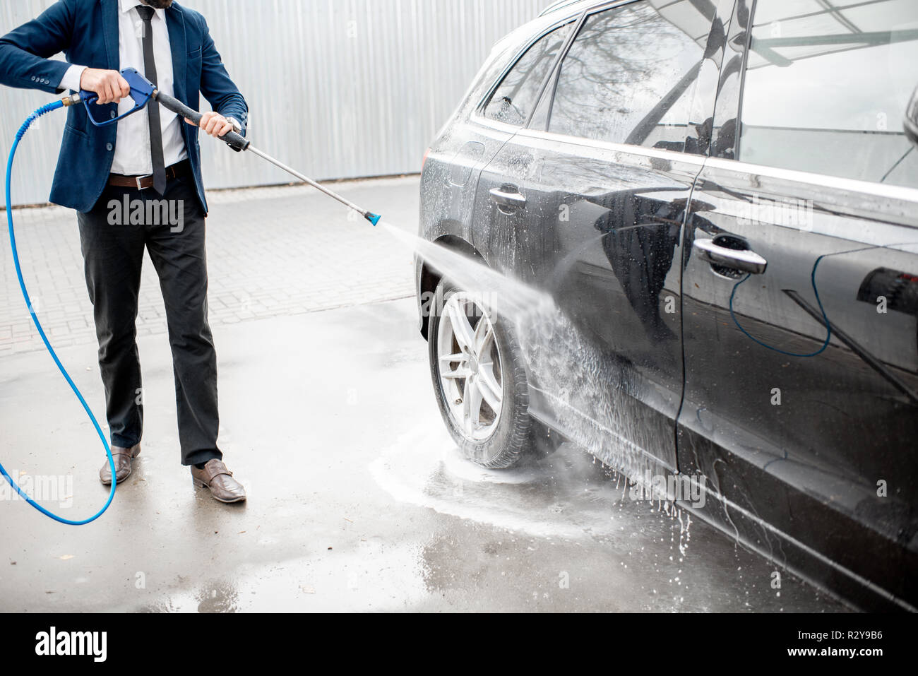 L'homme habillé en fonction de laver la voiture de luxe avec lave-gun sur un self service de lavage de voiture en plein air Banque D'Images