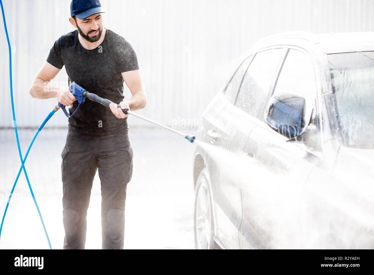 Rondelle professionnel en uniforme noir lave-voiture de luxe avec canon à eau sur un lavage de voiture en plein air Banque D'Images