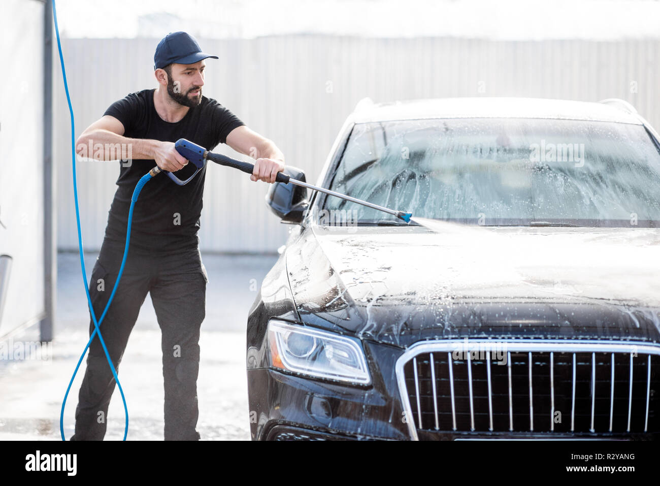 Rondelle professionnel en uniforme noir lave-voiture de luxe avec canon à eau sur un lavage de voiture en plein air Banque D'Images