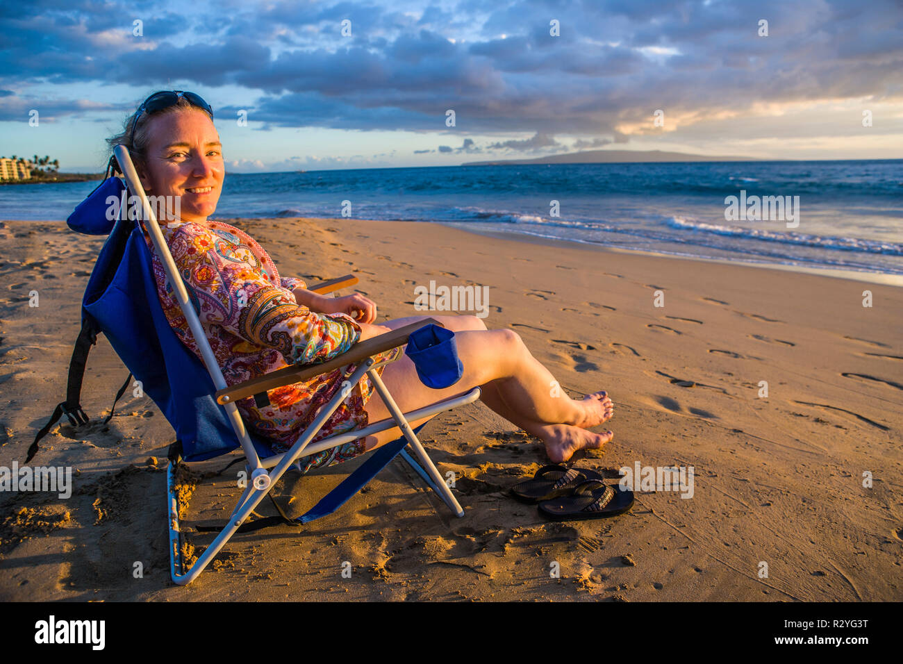 Une femme d'âge moyen assis sur une plage pour le coucher du soleil sur l'océan pacifique à Kihei, Maui, Hawaii, USA. Banque D'Images