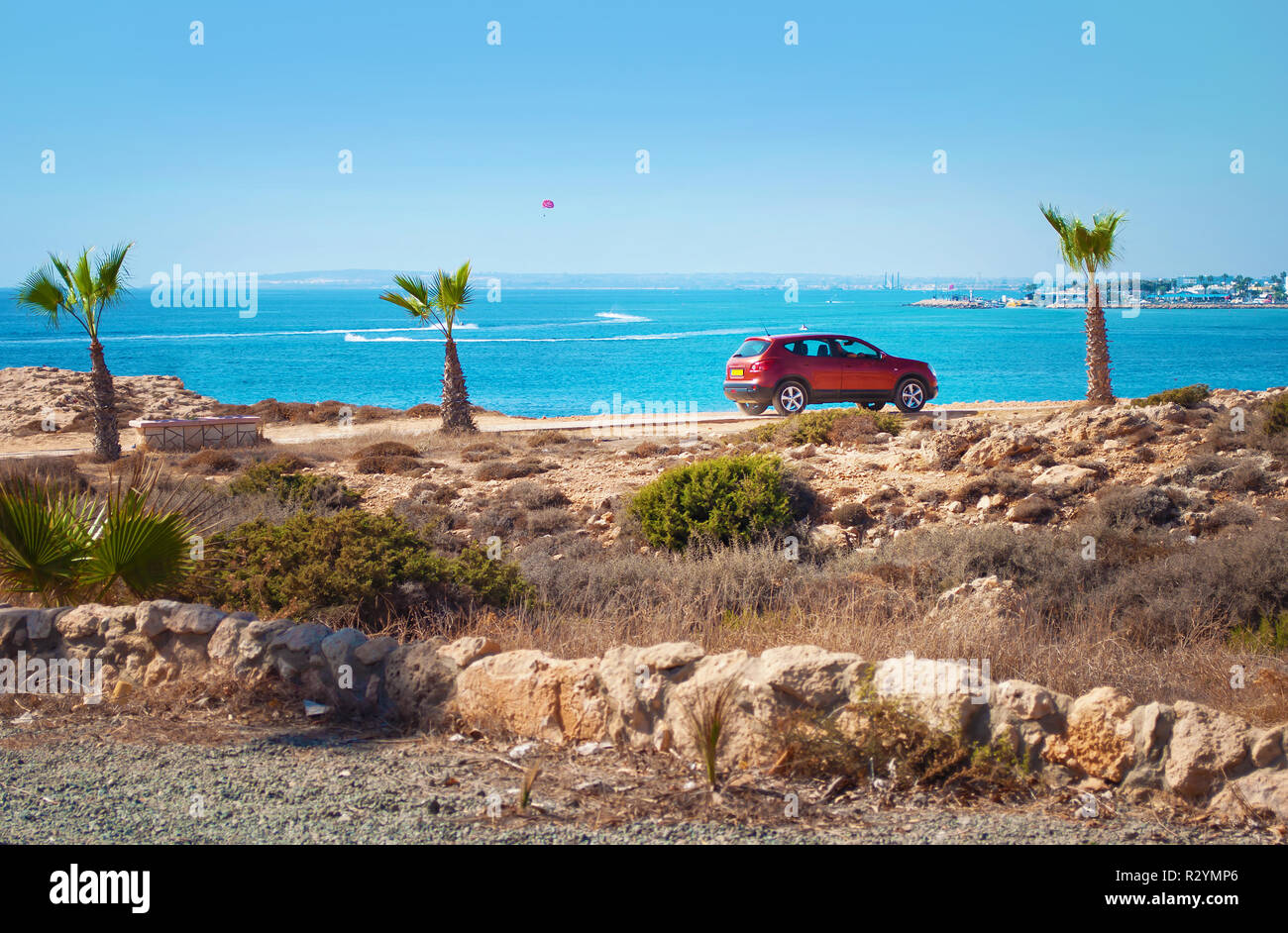 Une voiture berline rouge courte parmi les palmiers, buissons verts, et des pierres sur le fond bleu de la mer. Concept de voyages et de l'aventure, happ Banque D'Images