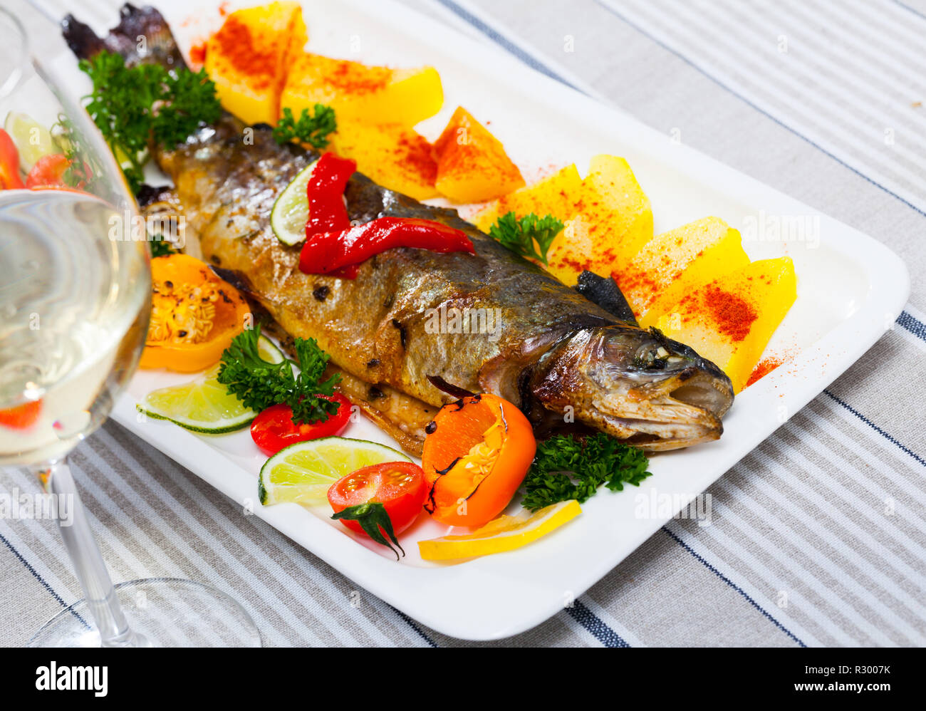 Truite au four délicieux servi sur une assiette avec des pommes de terre,  tomates, poivrons, verts, citron et vin blanc Photo Stock - Alamy