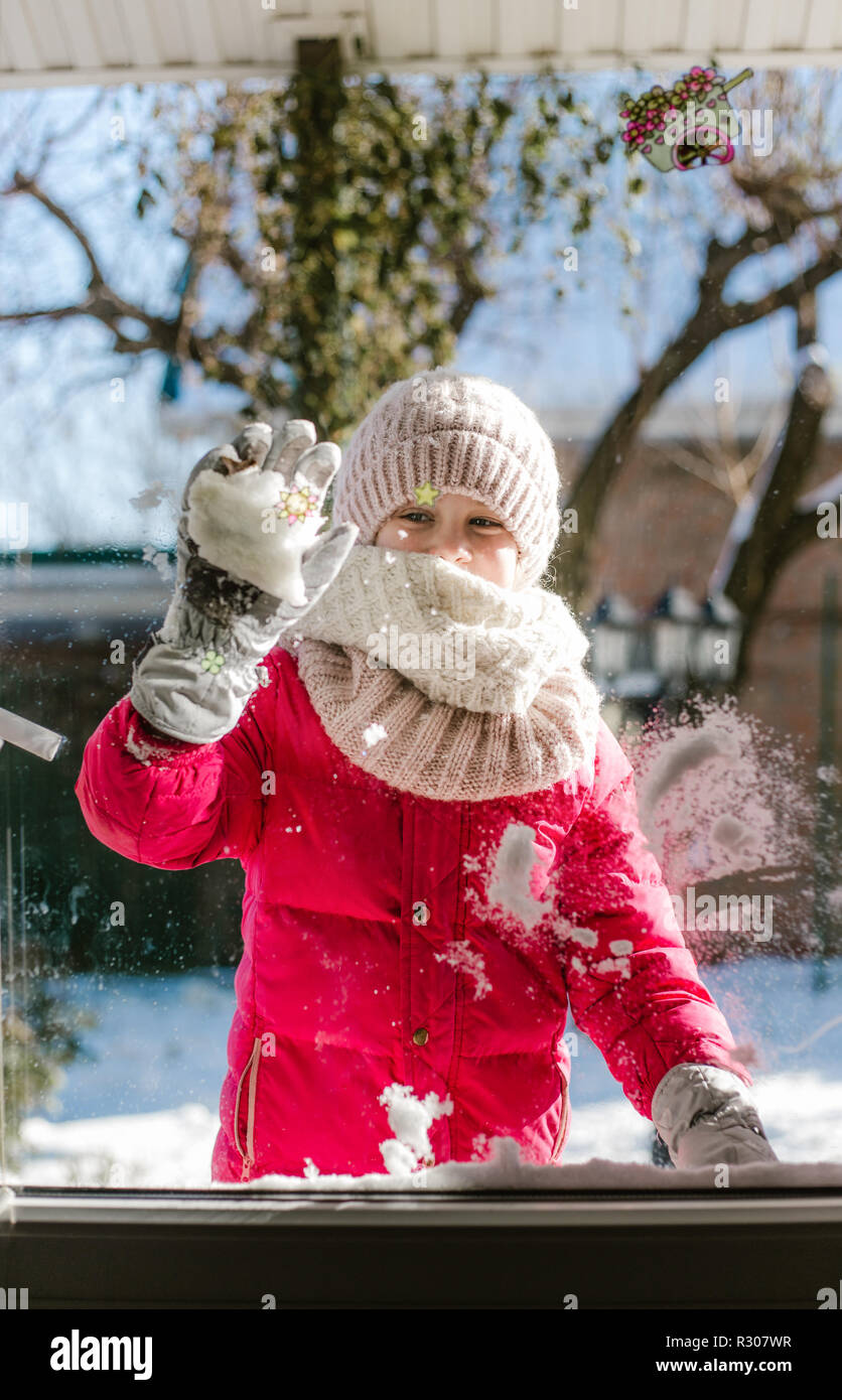 Sept ans, jolie fille dans des vêtements d'hiver se tient devant la porte, sur la rue avec de la neige dans ses mains et à la Chambre en souriant. Banque D'Images