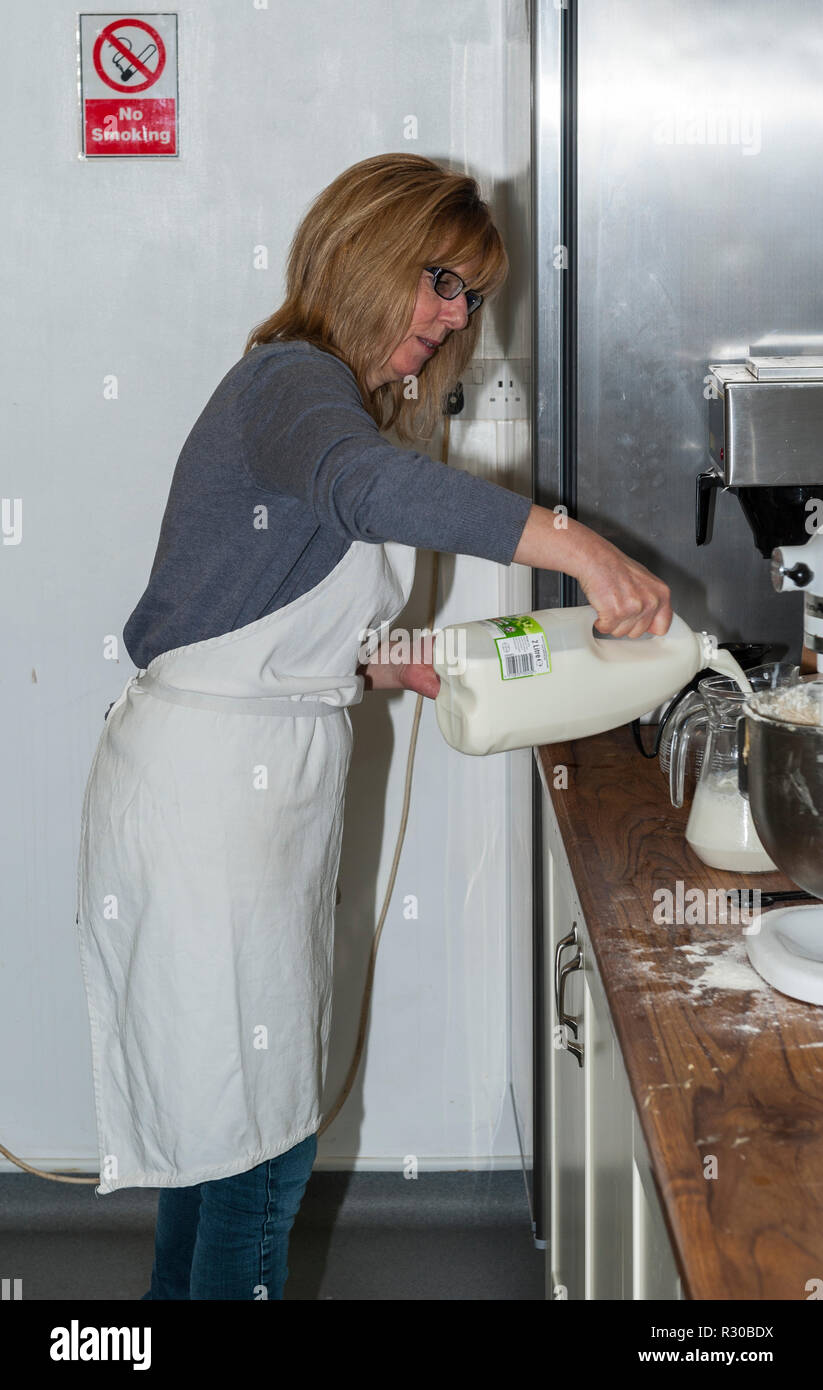Une femme versant du lait dans une cuisine industrielle au Royaume-Uni Banque D'Images