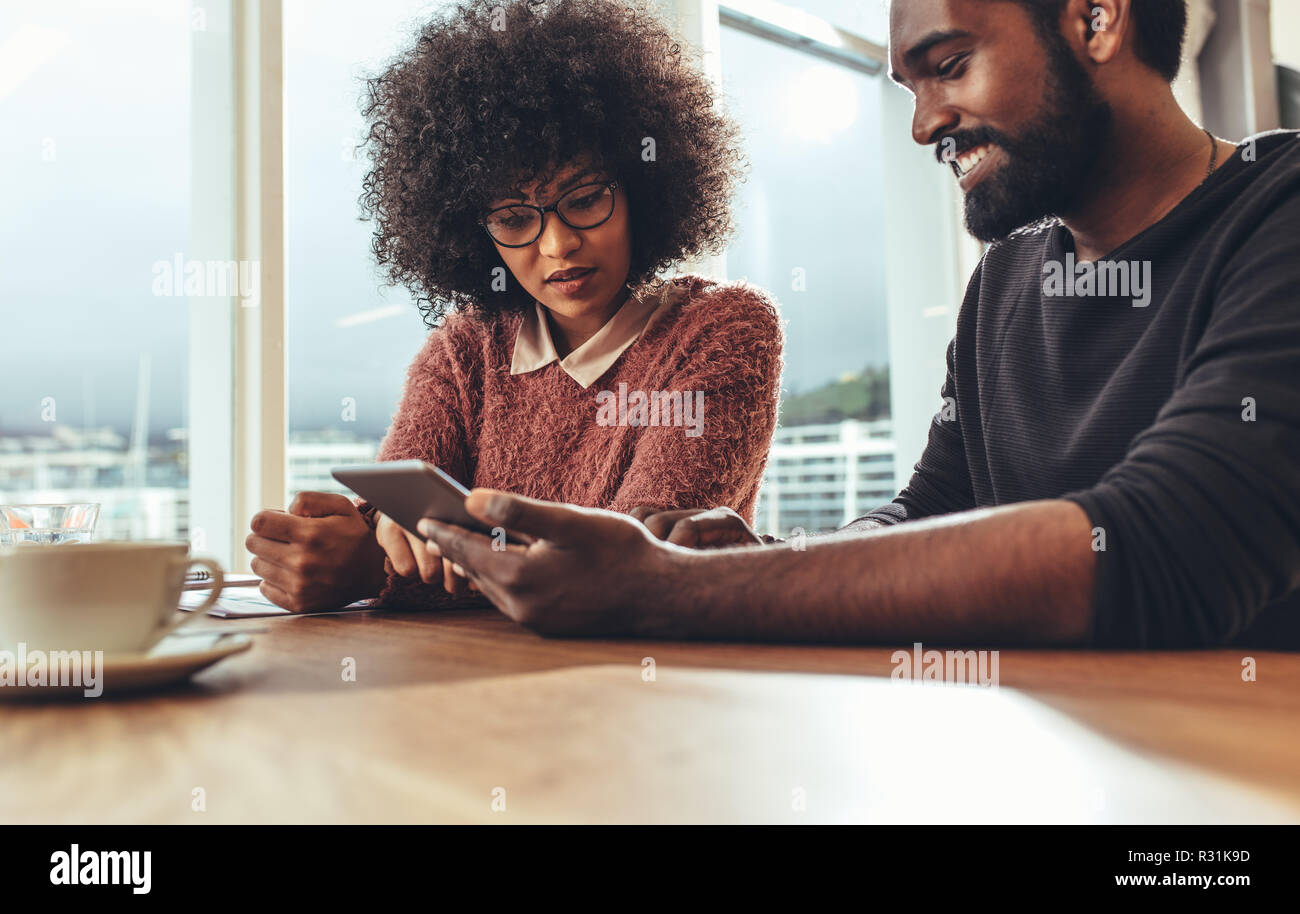 Hommes et femmes d'Afrique d'affaires l'échange d'idées au travail assis ensemble. Les collègues assis dans office looking at tablet pc avec une tasse de café sur Banque D'Images