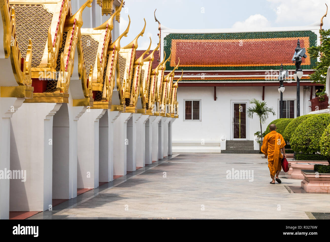 Un moine bouddhiste en robes orange marche dernières Wat Ratchanadda, Bangkok. Les 37 clochers tout métal symbolisent les 37 vertus qui mènent à l'illumination Banque D'Images