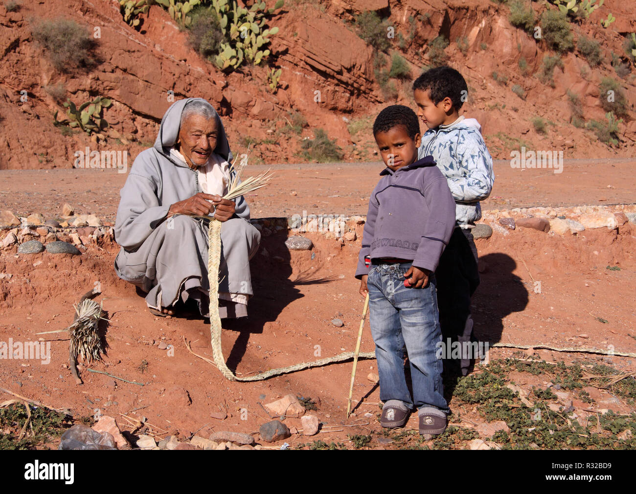Marrakech, Maroc - 21,02,2012 : Un vieil homme habillé en général, le berbère avec ses petits-enfants de l'artisanat les sangles du paille dans le Haut Atlas. Banque D'Images