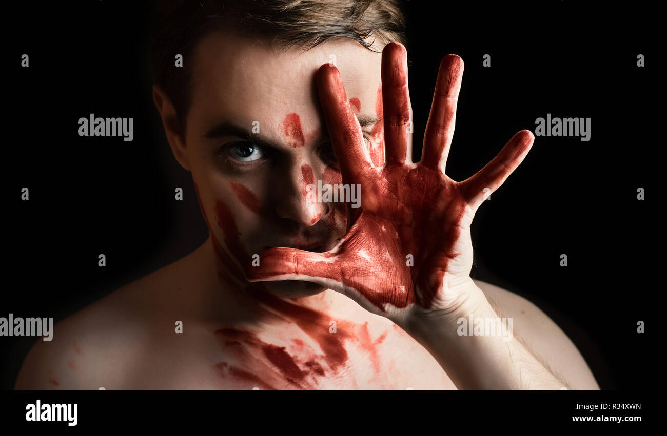 Portrait de jeune homme avec du sang sur son visage et palm sur fond sombre. Banque D'Images
