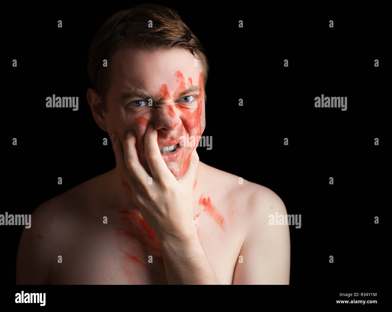 Portrait de jeune homme en colère avec de la peinture sur son visage sur fond sombre. Banque D'Images