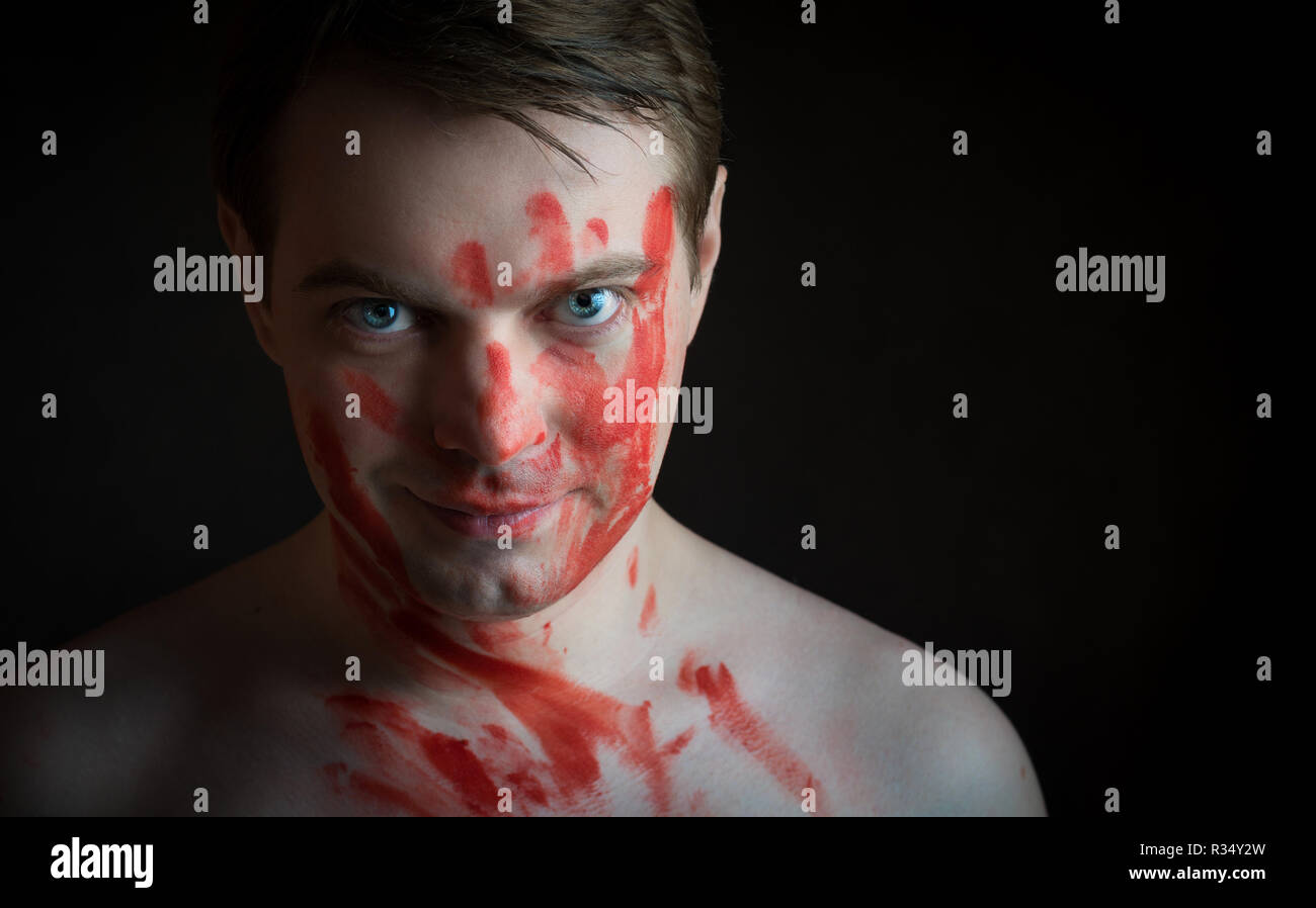 Portrait de jeune homme avec du sang sur son visage sur fond sombre. Banque D'Images
