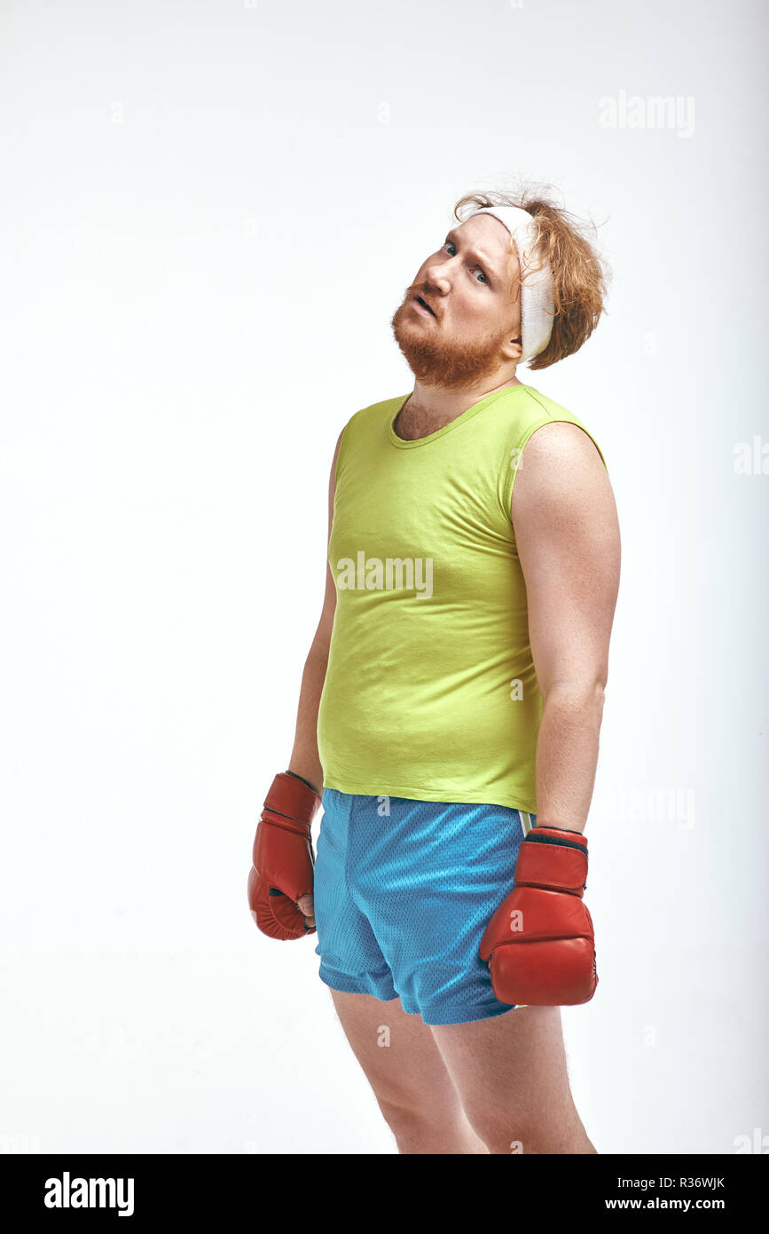 Fatigué, barbu, aux cheveux rouge dodu homme portant des vêtements de sport et des gants de boxe rouge Banque D'Images