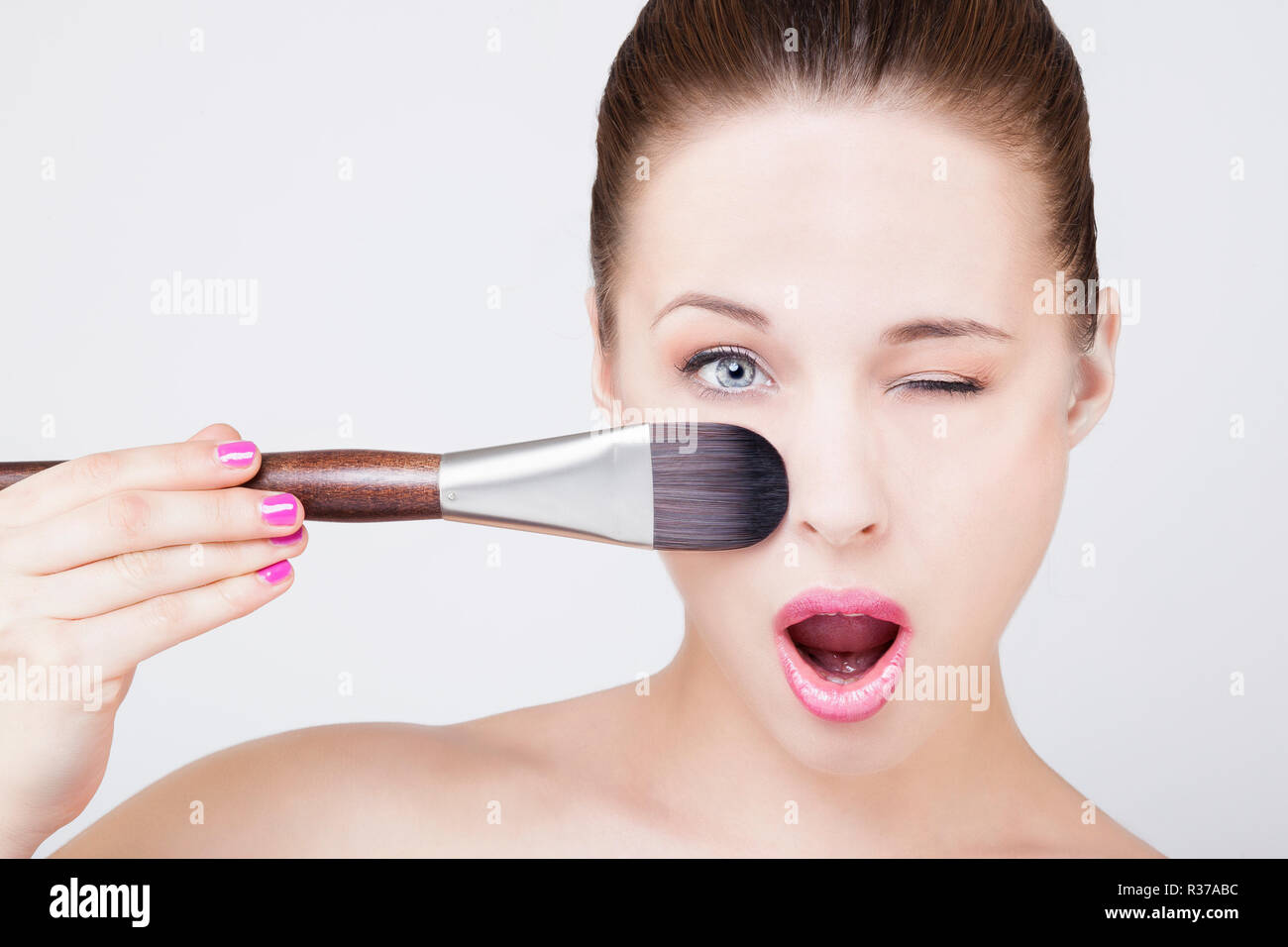Portrait of a young woman applying make-up une brosse sur son visage, clignant de l'oeil Banque D'Images