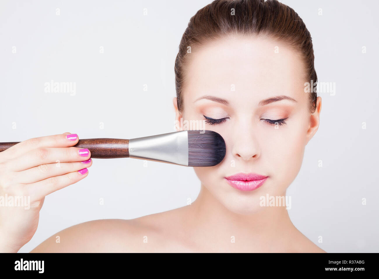 Portrait of a young woman applying make-up une brosse sur son visage, clignant de l'oeil Banque D'Images