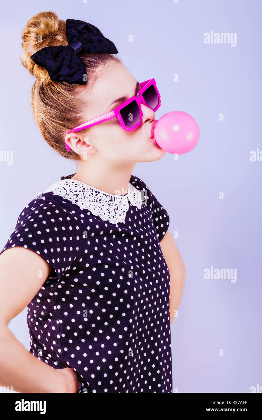 Profil humoristique d'une jeune femme faisant une bulle de chewing-gum, les mains sur les hanches Banque D'Images