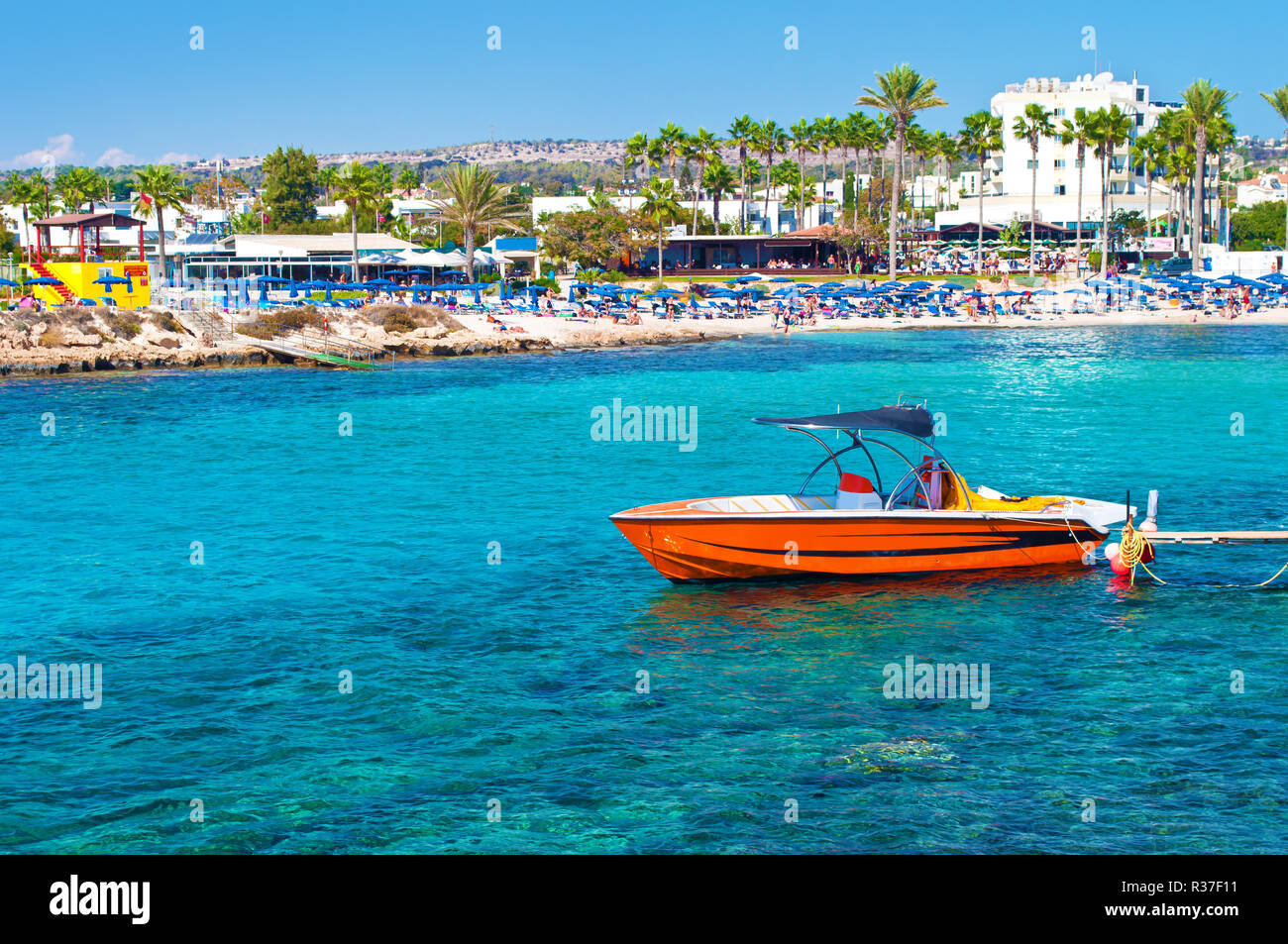 Image d'un hors-bord rouge près de Vathia Gonia beach près de Agia Napa, Chypre. Avec la mer bleu turquoise de l'eau, de nombreux espaces verts palmiers, maisons sur le background Banque D'Images
