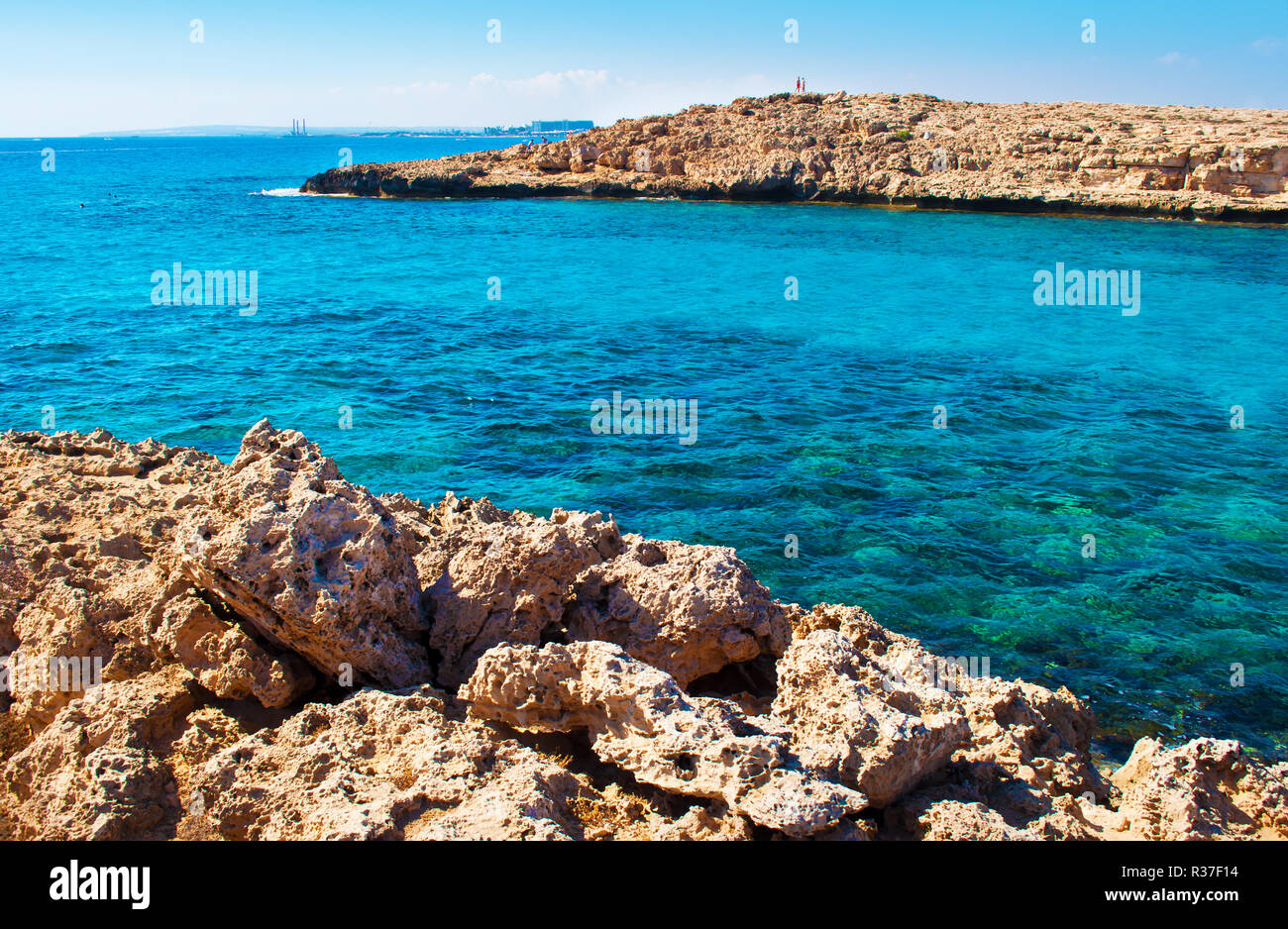 Image d'une baie près de plage Vathia Gonia, Agia Napa, Chypre. Littoral calcaire rugueux près de l'eau d'un bleu profond et les chiffres de deux personnes sur une colline rocheuse sur Banque D'Images