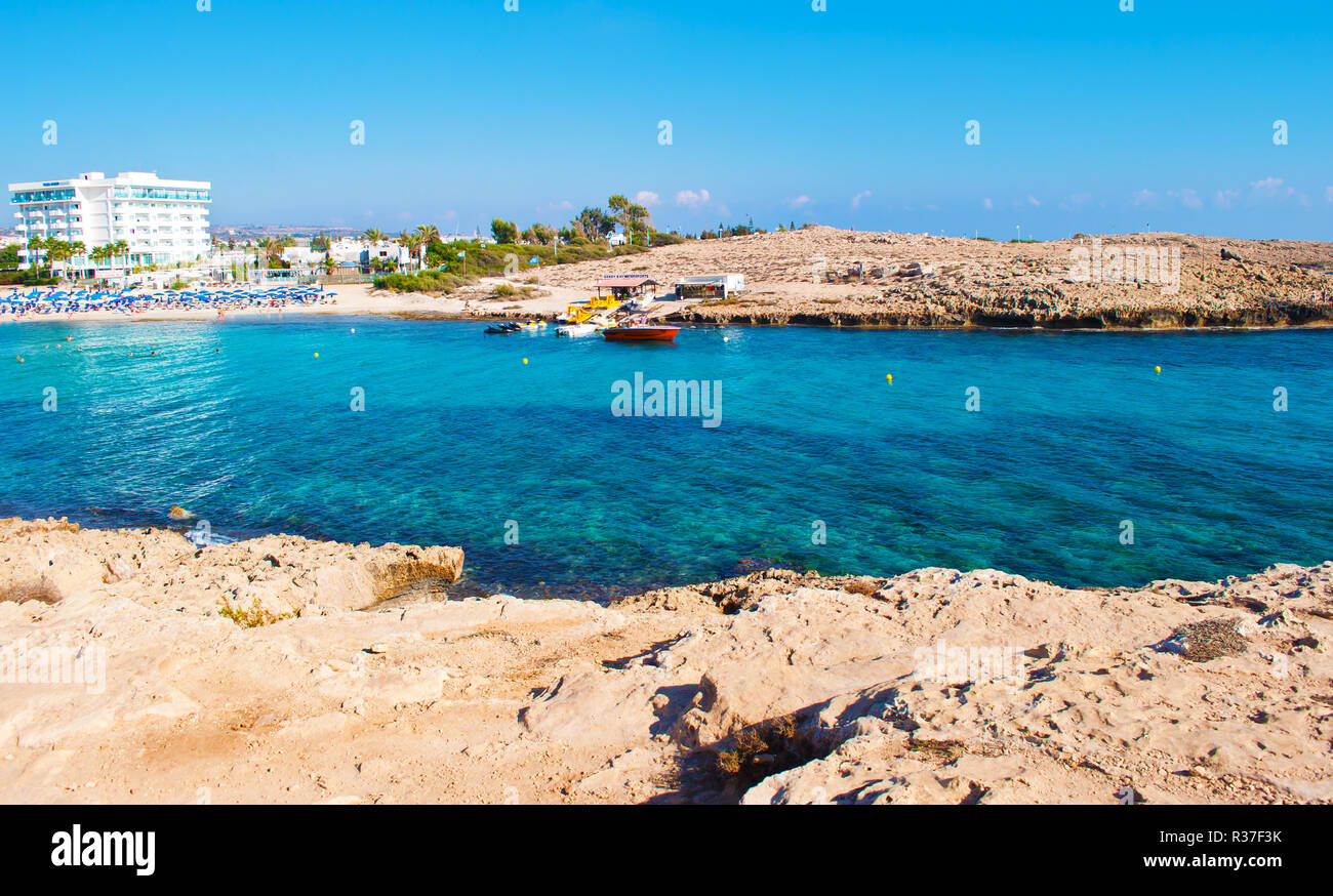 Image d'une baie près de plage Vathia Gonia, Agia Napa, Chypre. Près de la Côte calcaire rugueux transparent bleu profond de l'eau et un bateau contre orange rock Banque D'Images
