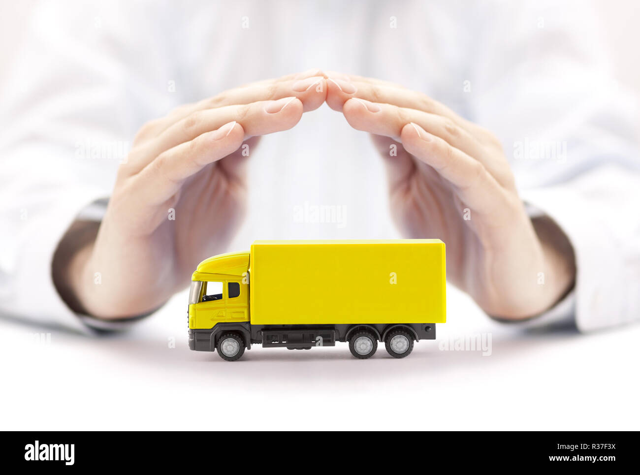 Assurance auto. Miniature camion jaune couverte par les mains. Banque D'Images