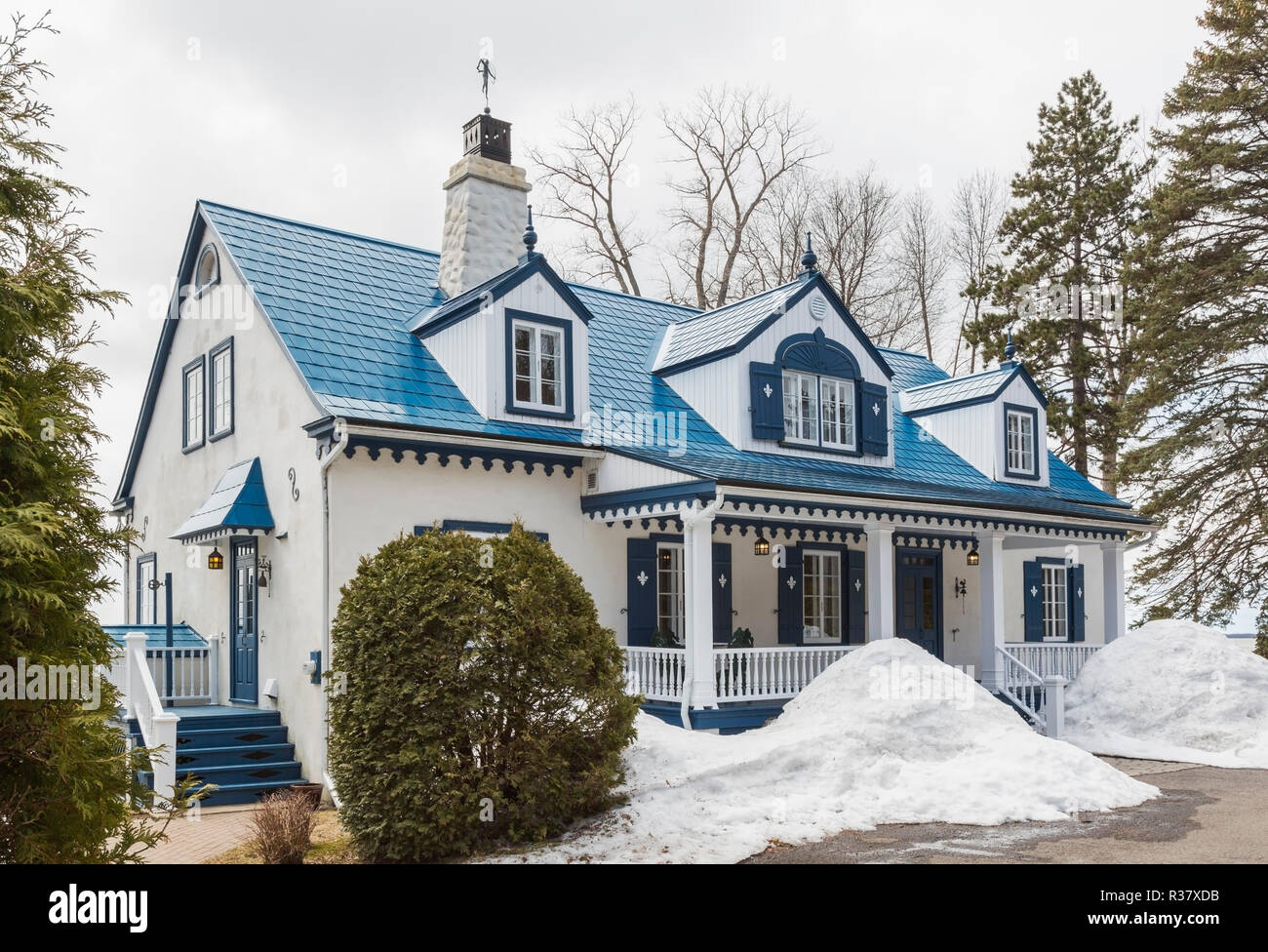1920 ancien crépi blanc avec garniture bleue style chalet avec façade maison en tuiles acier bleu au début du printemps, Québec, Canada Banque D'Images
