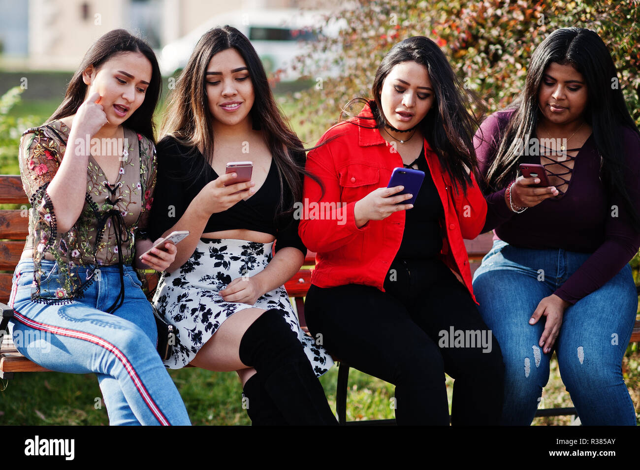 Groupe de quatre professionnels et de jolies filles de latino Equateur posés au niveau de la rue qu'à la recherche de téléphones mobiles. Banque D'Images