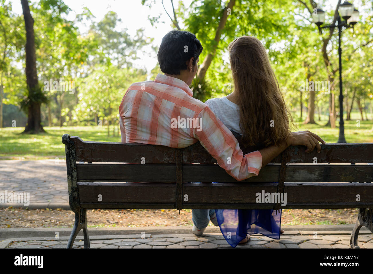Vue arrière de multi ethnic couple assis sur banc en bois dans l'amour Banque D'Images