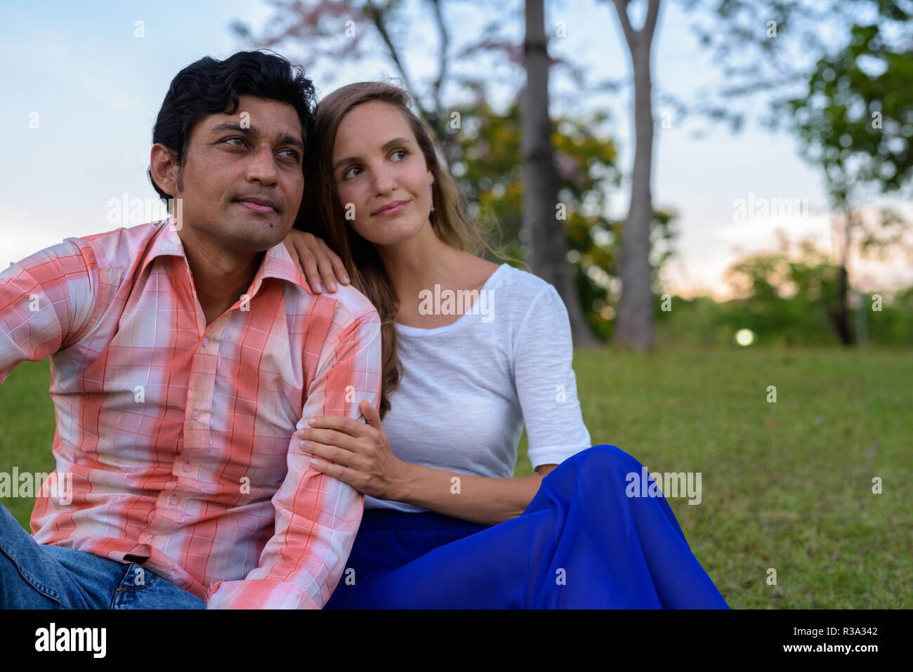 Multi Ethnic couple sitting et de penser sur la prairie dans l'amour un Banque D'Images