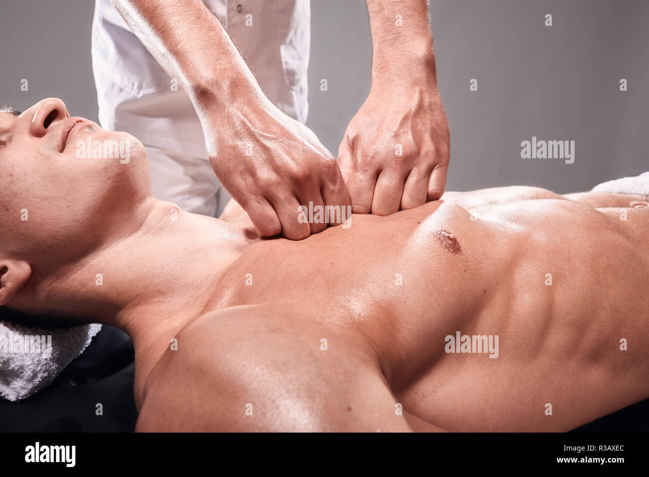 Vue de côté, deux jeune homme, 20-29 ans, physiothérapie sportive à l'intérieur en studio, séance photo. Massage masseur sportif mans poitrine, corps musclé, h Banque D'Images