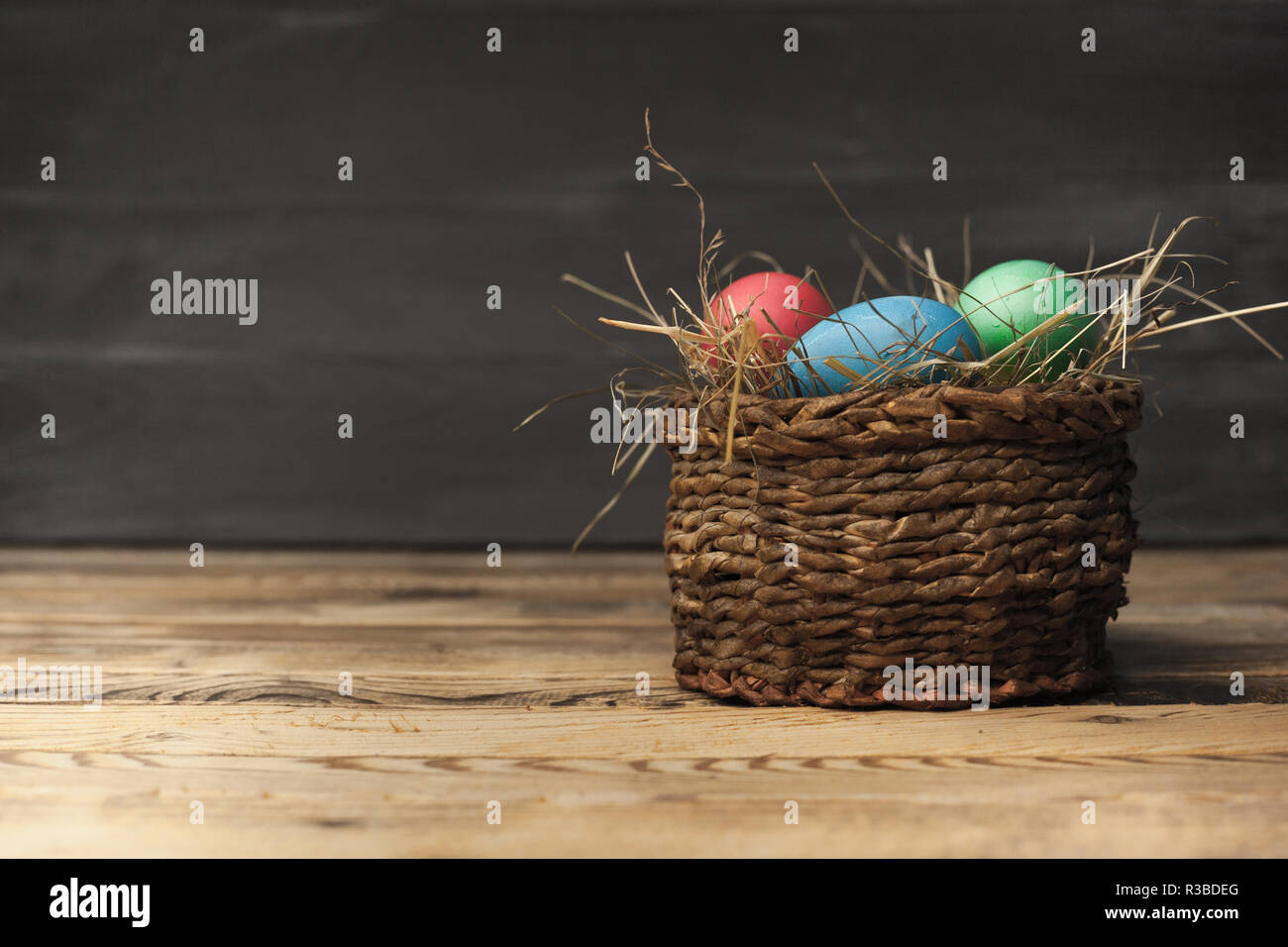 Les oeufs de pâques de diverses couleurs dans un panier en osier avec du foin sur un fond de bois Banque D'Images