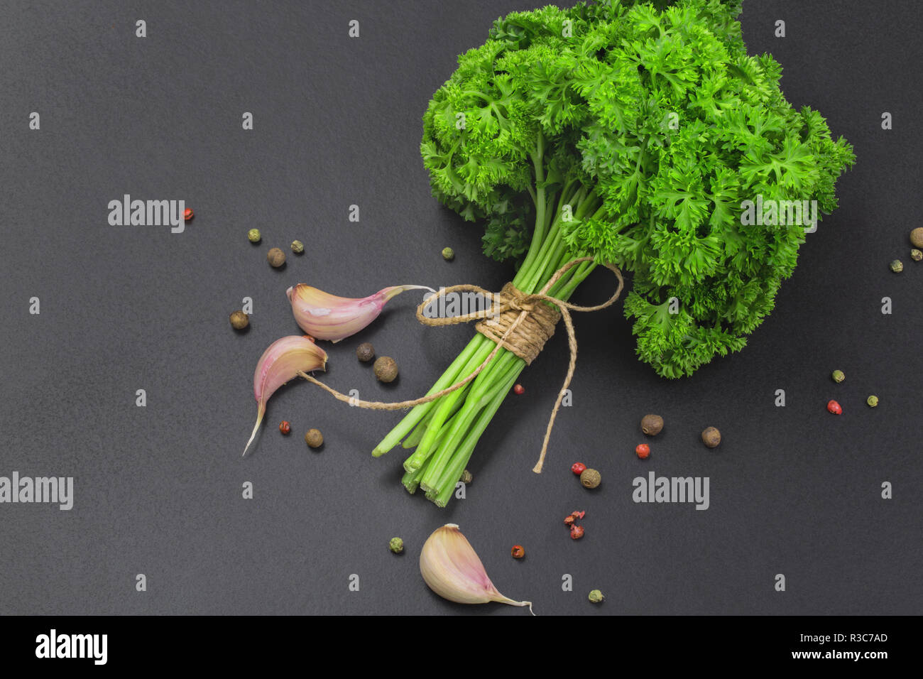 Un bouquet de persil frais bandé avec une corde avec un arc et un mélange d'épices et l'ail sur un tableau noir, vue du dessus Banque D'Images