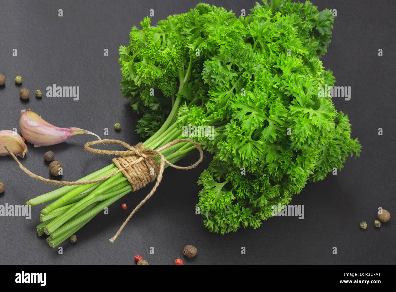 Un bouquet de persil frais bandé avec une corde avec un arc et un mélange d'épices et l'ail sur un tableau noir, vue du dessus Banque D'Images