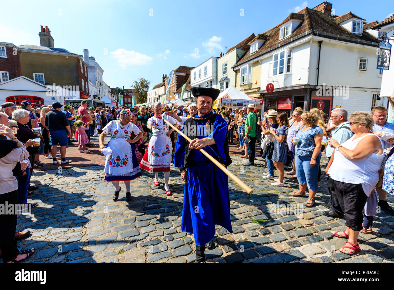 Faversham hop festival, Parade. Balaton danseurs hongrois, le plomb par l'homme en robe bleue, marche dans la rue bondée de spectateurs à regarder. Banque D'Images