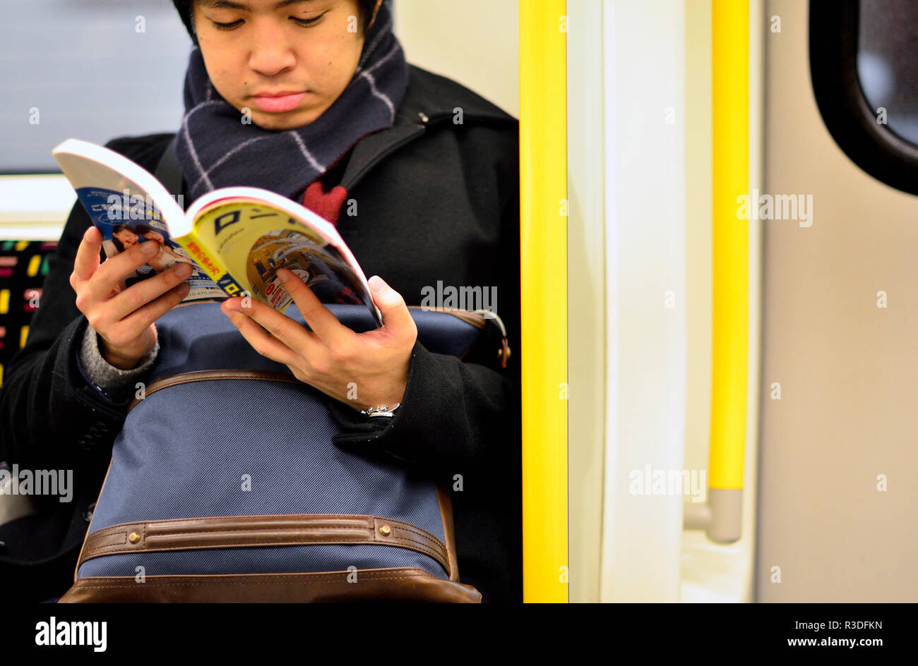 Jeune homme japonais Hentai la lecture d'un roman graphique sur un train de tube, Londres, Angleterre, Royaume-Uni. Banque D'Images