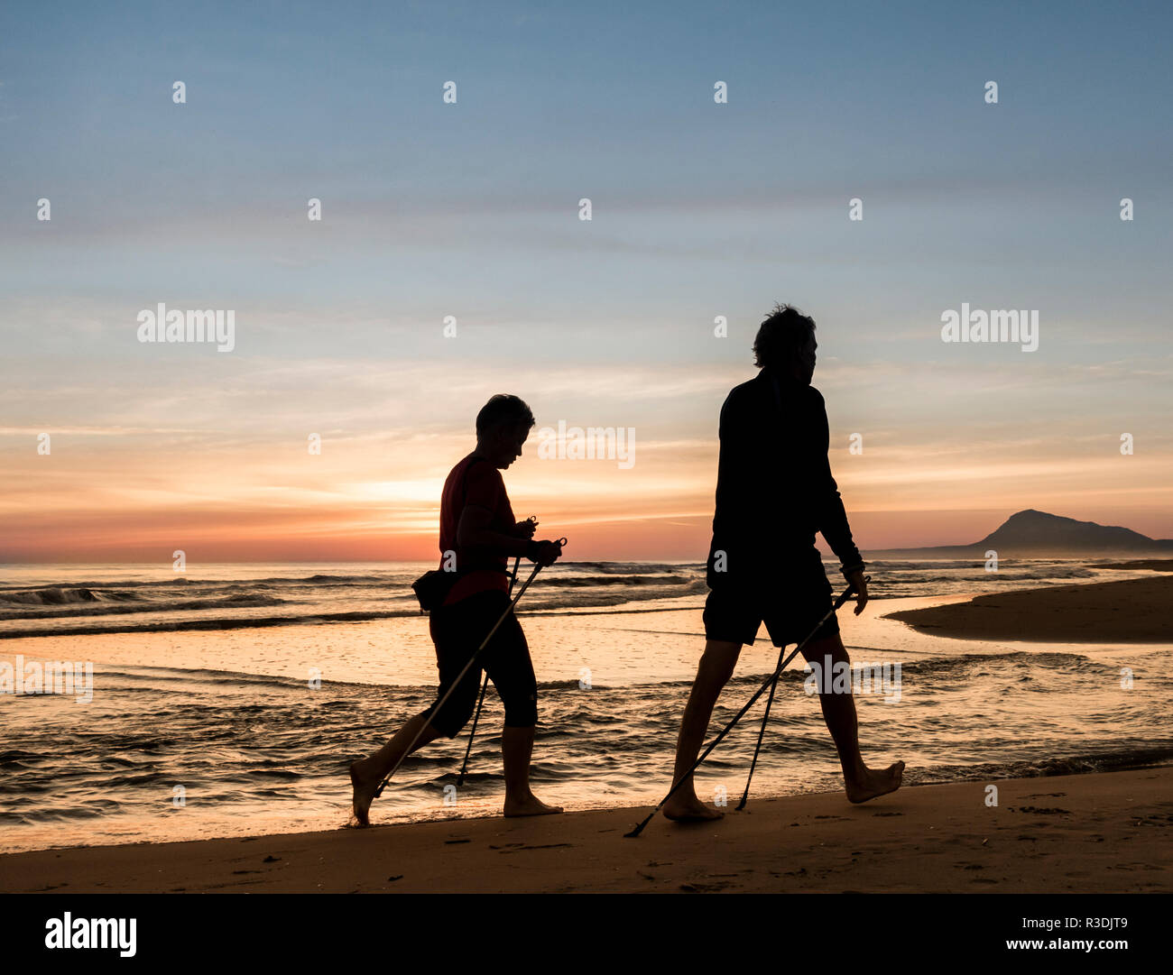 Mature couple walking avec poteaux, marche nordique, sur la plage au lever du soleil en Espagne. Banque D'Images