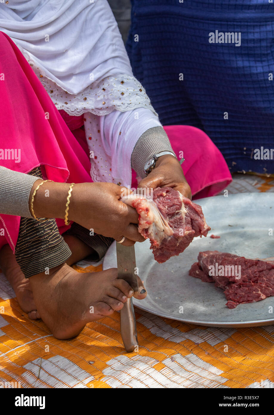 Harari femme couper la viande avec un couteau qu'elle tient avec son pied, Harari, Harar, Éthiopie Région Banque D'Images