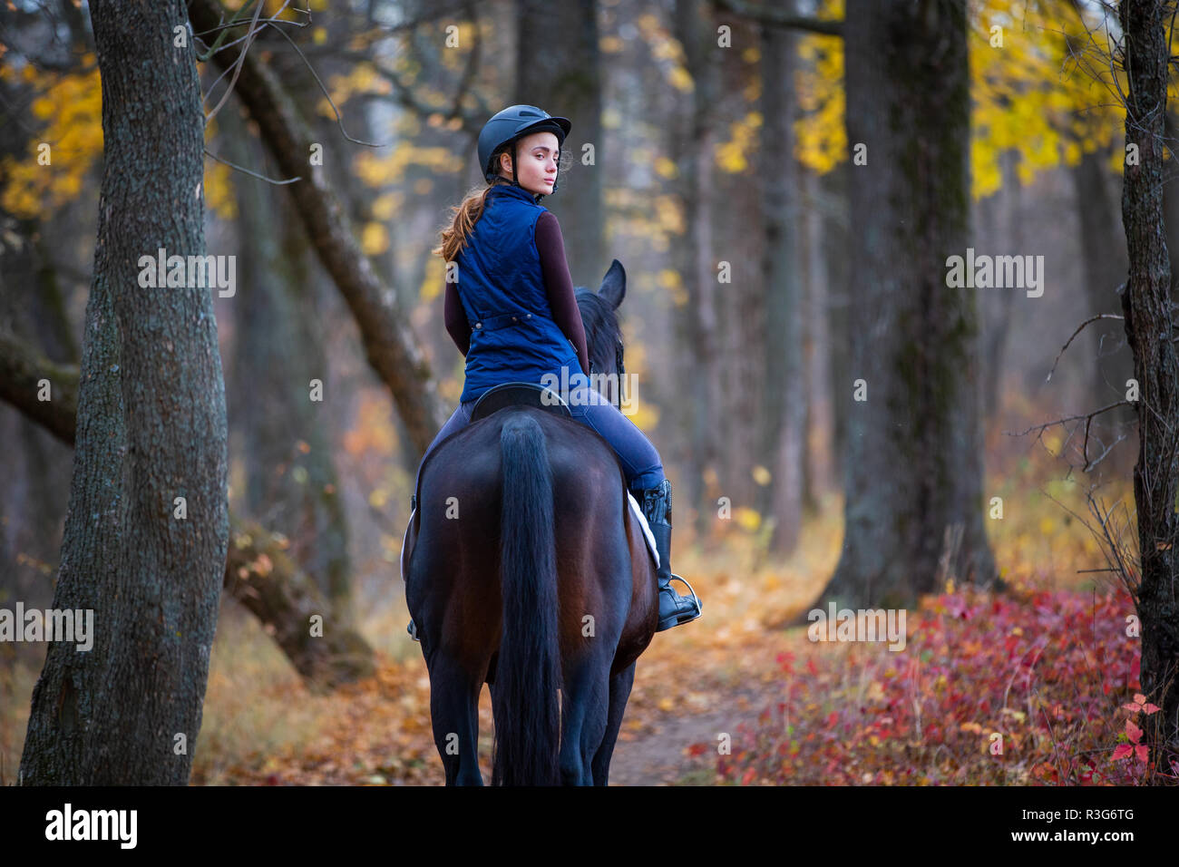 Teenage girl riding horse in autumn park. Happy rider avec son étalon sur la marche Banque D'Images