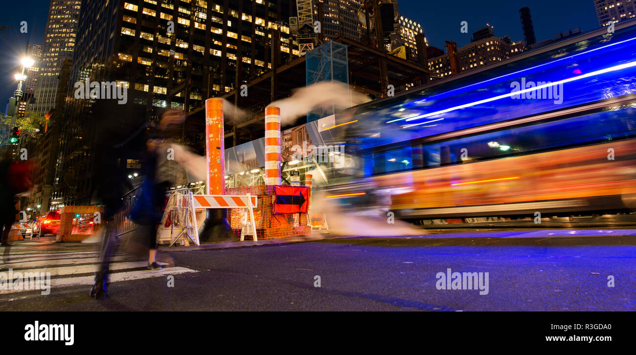 Une longue exposition photo de bus et les personnes qui traversent une intersection à New York pendant que la vapeur qui sort du trou. Banque D'Images