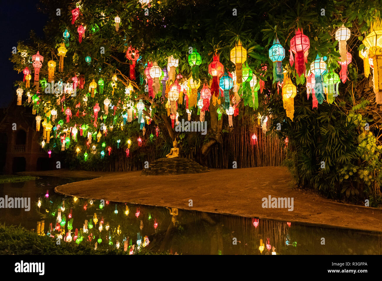 Lanternes feu colorés entourent statue de Bouddha près de pond à la réflexion. Banque D'Images