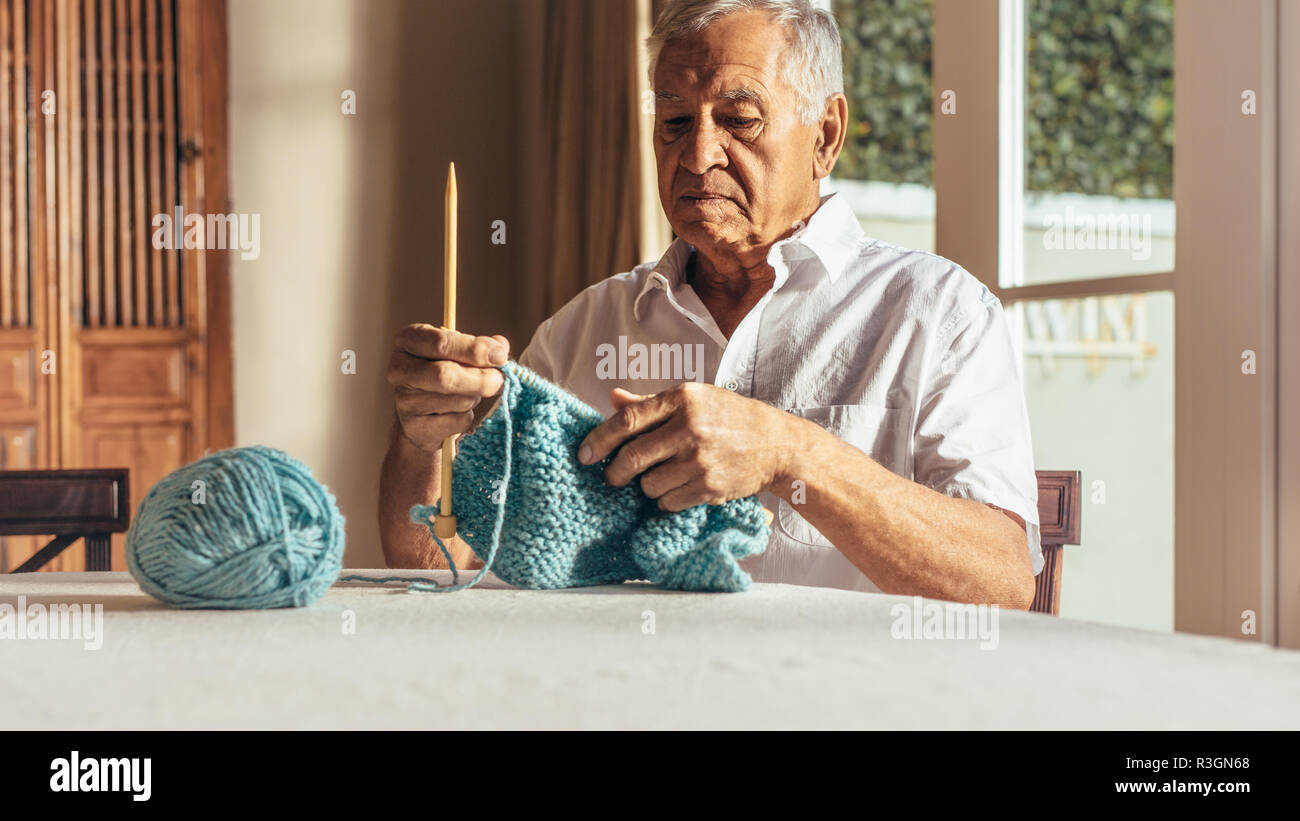 Man knitting vêtements chauds avec fil de laine sur table. L'homme à la retraite faisant un pull avec des aiguilles et fil de laine à la maison. Banque D'Images