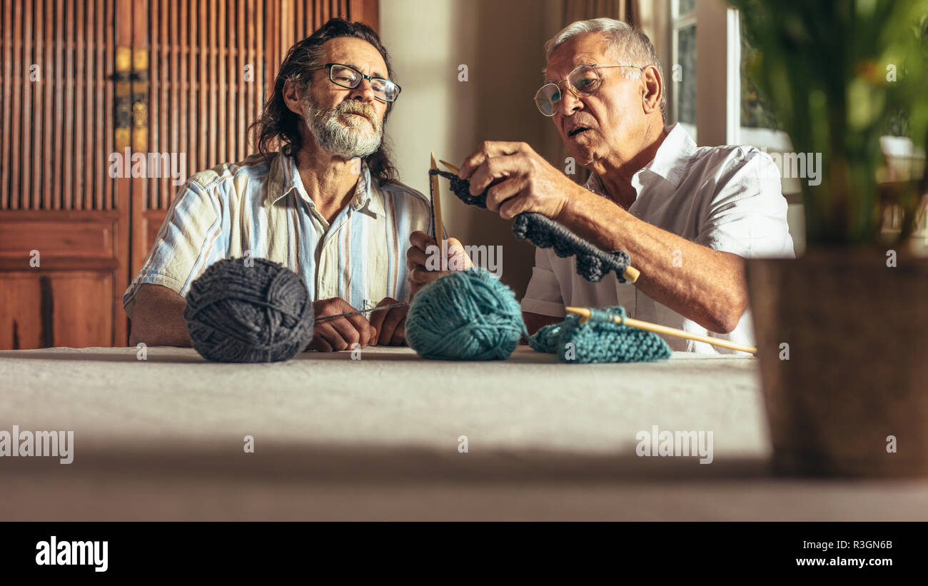 L'homme principal enseignant ses amis l'art de vêtements de laine à tricoter. Man apprendre à tricoter des vêtements en laine de ses amis assis à la maison. Banque D'Images