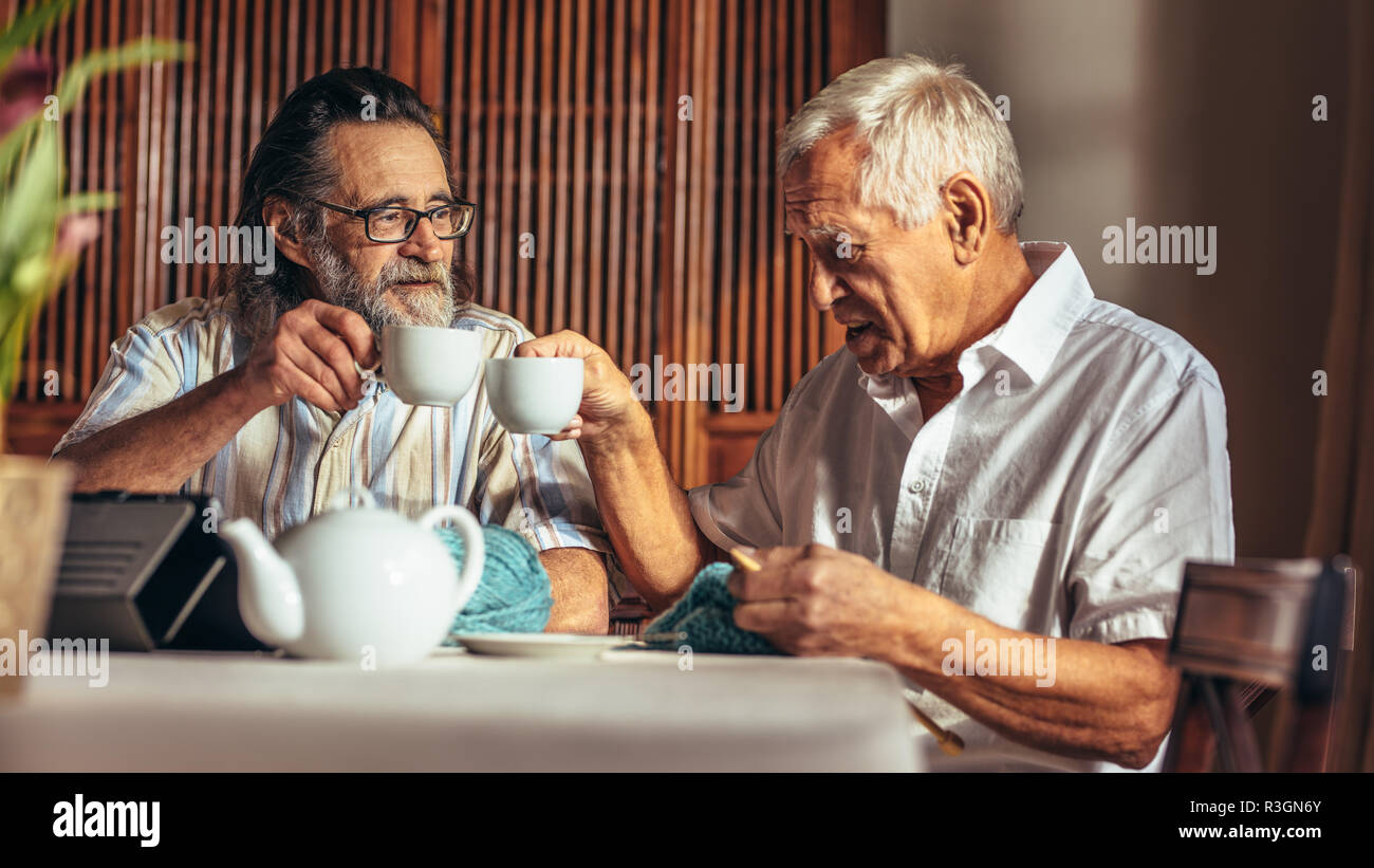 Les hommes à la retraite tout en prenant le thé à la maison de tricot. Deux hauts men toasting cups thé tout en étant assis à table à la maison. Banque D'Images