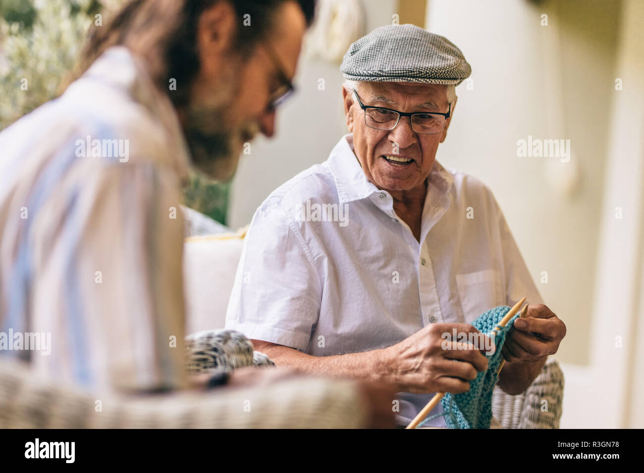 Man hat en regardant son ami tricot faire assis à une terrasse. Amis des hommes âgés le kitting ensemble. Banque D'Images