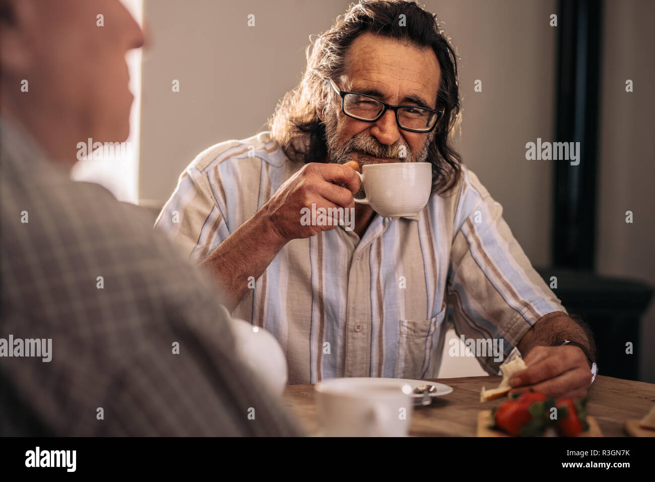 Deux hommes ayant le souper ensemble à la maison. Un homme âgé assis avec ami prenant le thé et des collations à l'intérieur. Banque D'Images
