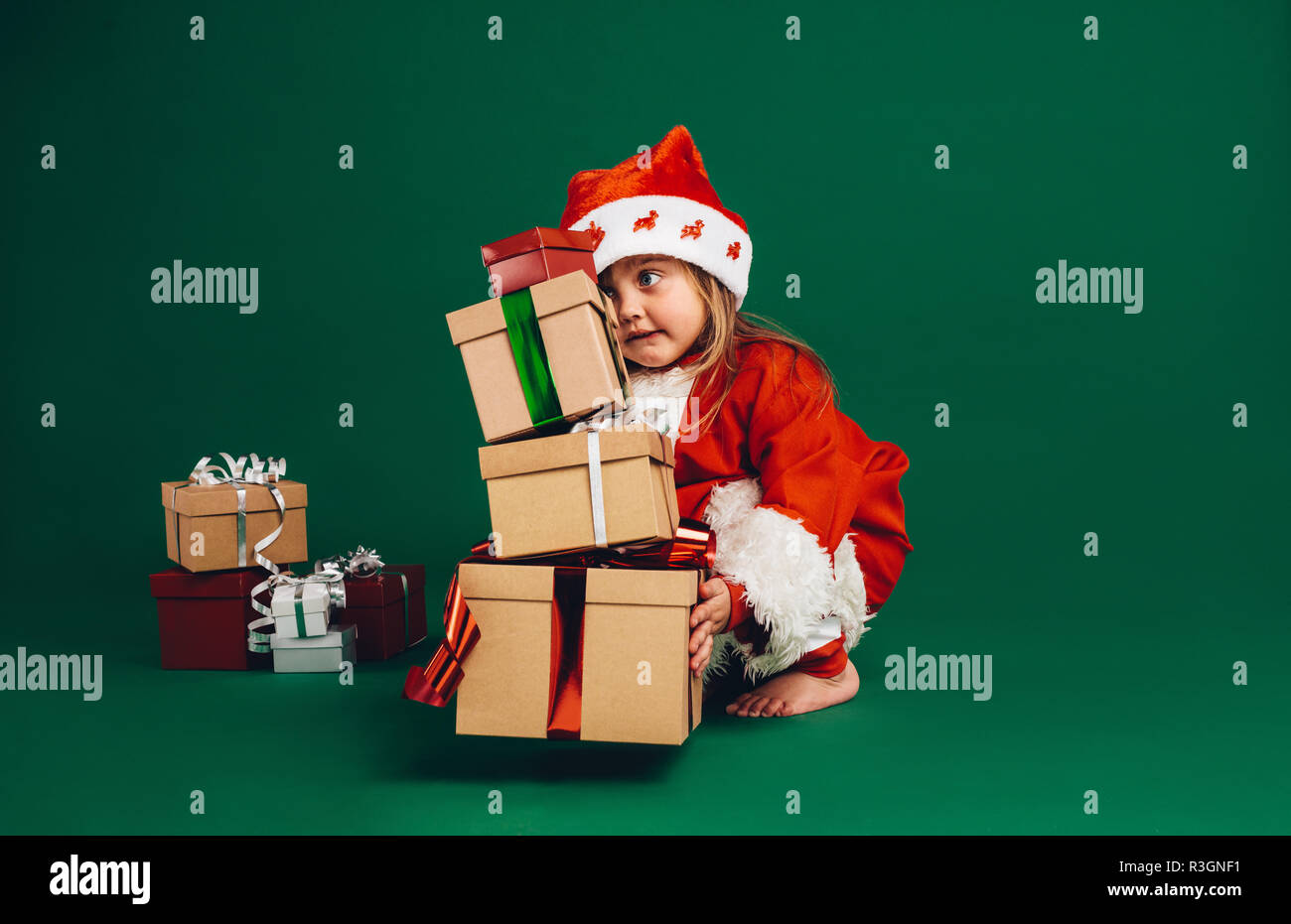 Petite fille au père Noël dress levée une pile de boîtes cadeaux. Kid à santa costume jouant avec les coffrets cadeaux. Banque D'Images