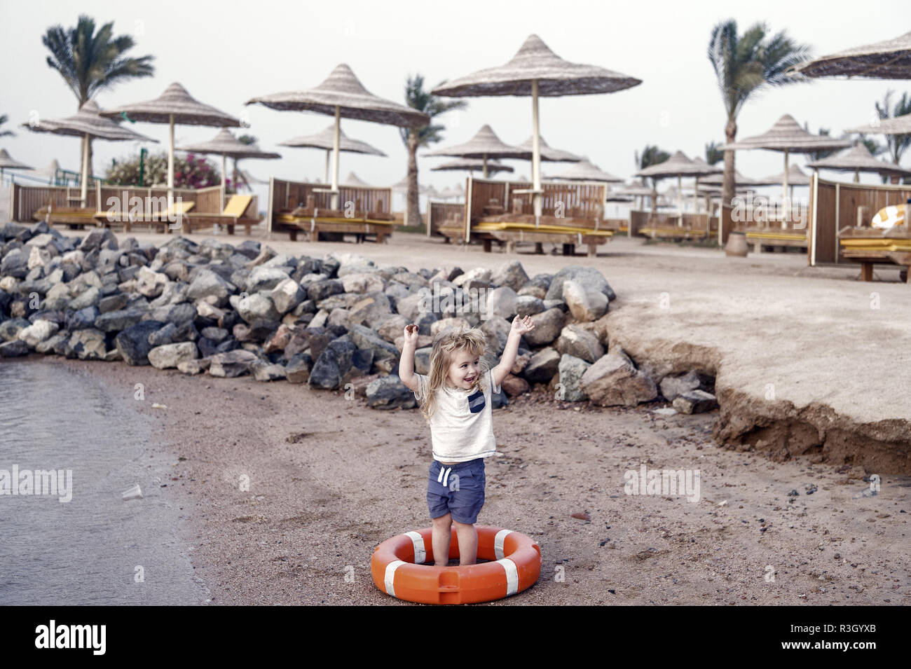 Petit Garcon De Bebe Ou Enfant Mignon Visage Heureux Et Avec Des Cheveux Blonds En Shirt Short Et Pieds Nus Jouant Avec La Ceinture Rouge Ou Bouee A Sandy Beach Wit Photo