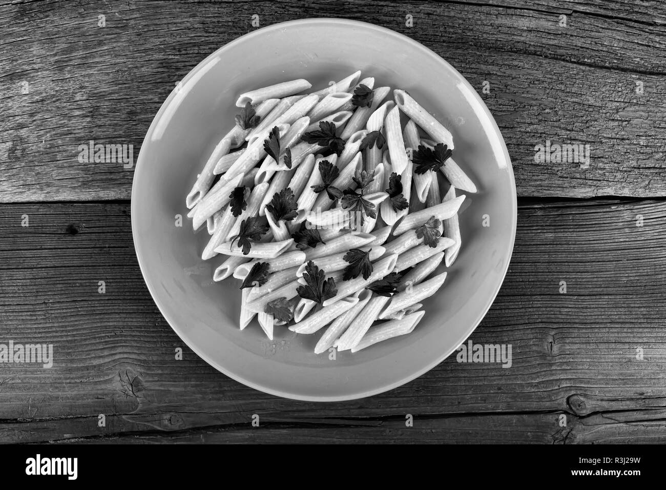 Photo en noir et blanc. L'Italien pâtes penne avec des feuilles de coriandre. Plat Bleu sur une table en bois. Vue de dessus, style rustique Banque D'Images