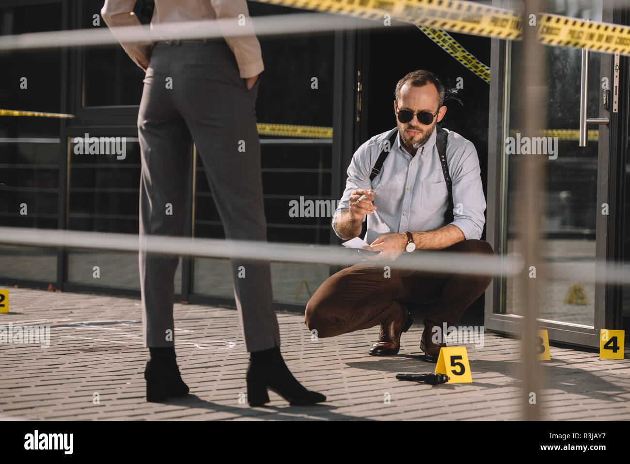 Homme assis à fumer et lunettes de détective à la scène de crime au partenaire avec près de lui Banque D'Images