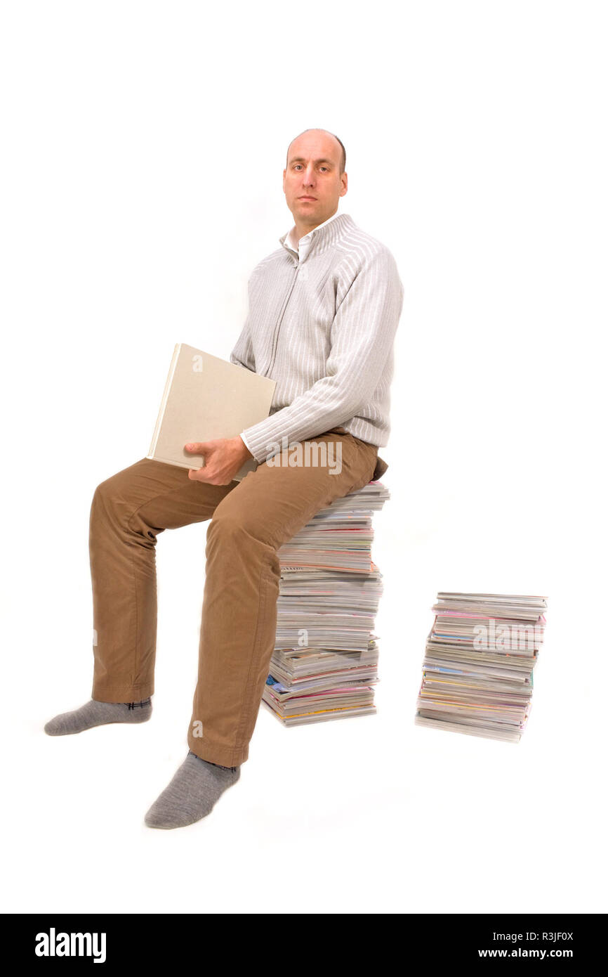 Homme assis sur une pile de magazines et en regardant un livre Banque D'Images