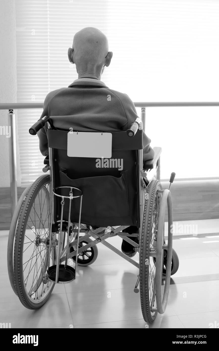 Vue arrière de senior man in wheelchair at hospital hallway Banque D'Images
