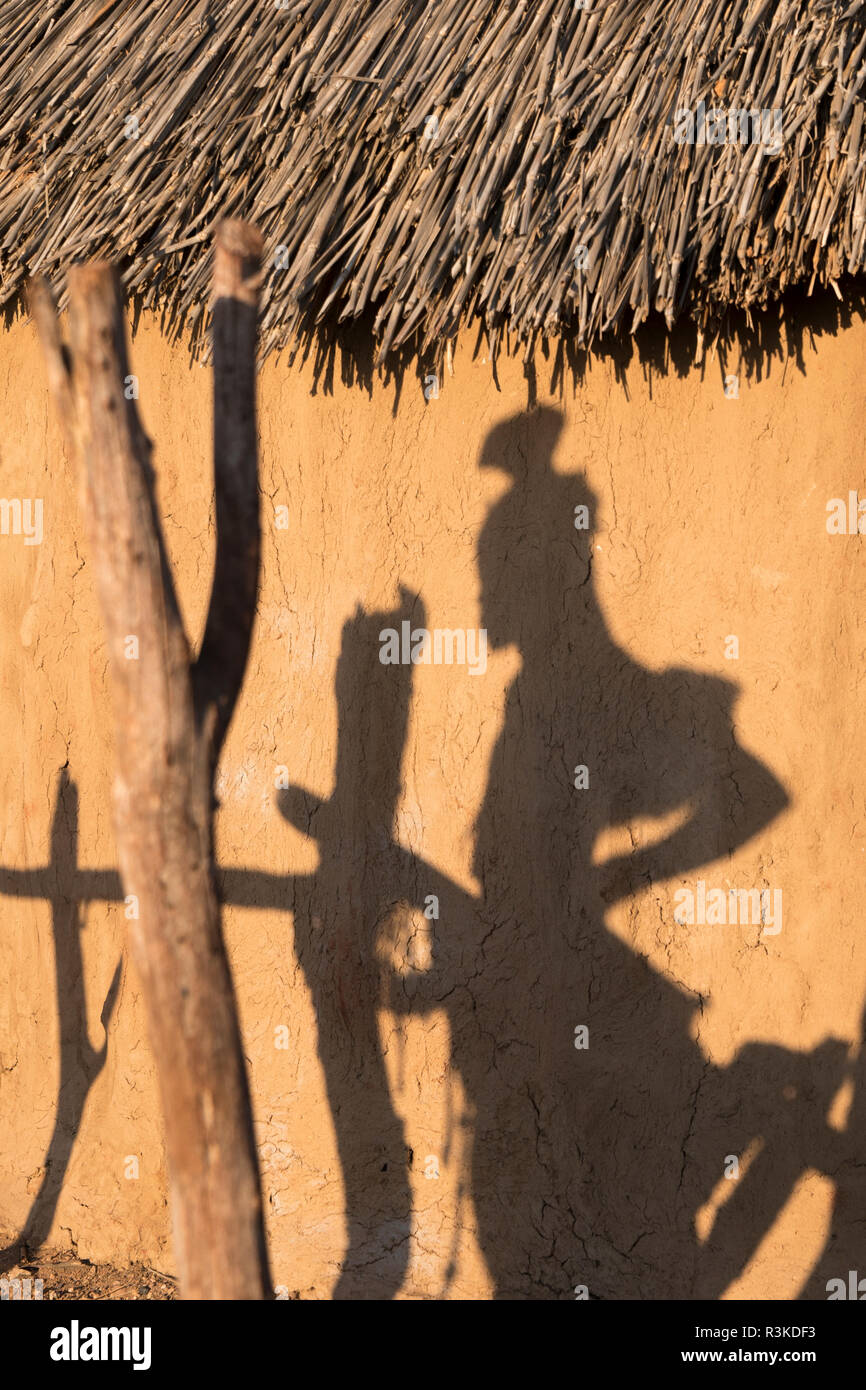 Ombre d'une femme Himba sur le côté d'une hutte de village dans un village près d'Opuwo. Banque D'Images