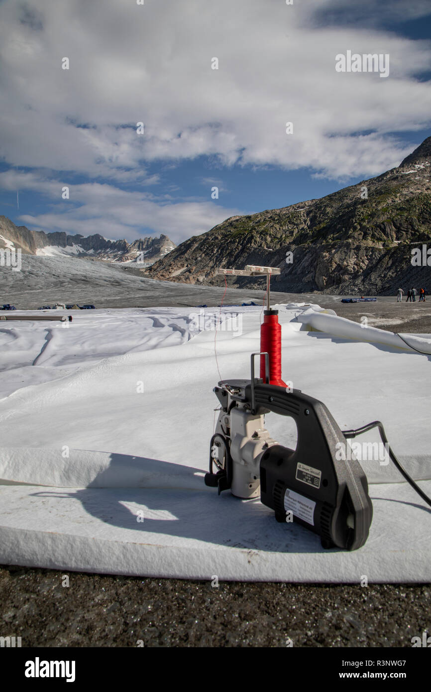 Climat | Albedo | Rhone : machine à coudre à main utilisée pour assembler d'énormes couvertures en polaire afin d'empêcher la fonte du tunnel de glace populaire à l'embouchure du glacier du Rhône. Après un hiver avec des quantités record de neige, la plupart de cette photo a disparu lorsque cette photo a été prise le 14 juillet 2018, exposant la glace plus sombre. Alors que la neige est un brillant réflecteur de l'énergie du soleil, la glace plus sombre absorbe l'énergie, accélérant ainsi la fonte du glacier. La couleur et l'obscurité de la glace du glacier varient partout dans le monde, selon l'accumulation de pollution, l'âge de la glace, les particules récupérées par Banque D'Images